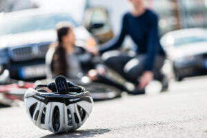 Close-up of a bicycling helmet fallen down on the ground after accidental collision between bicycle and a 4x4 car with injured victim in the background